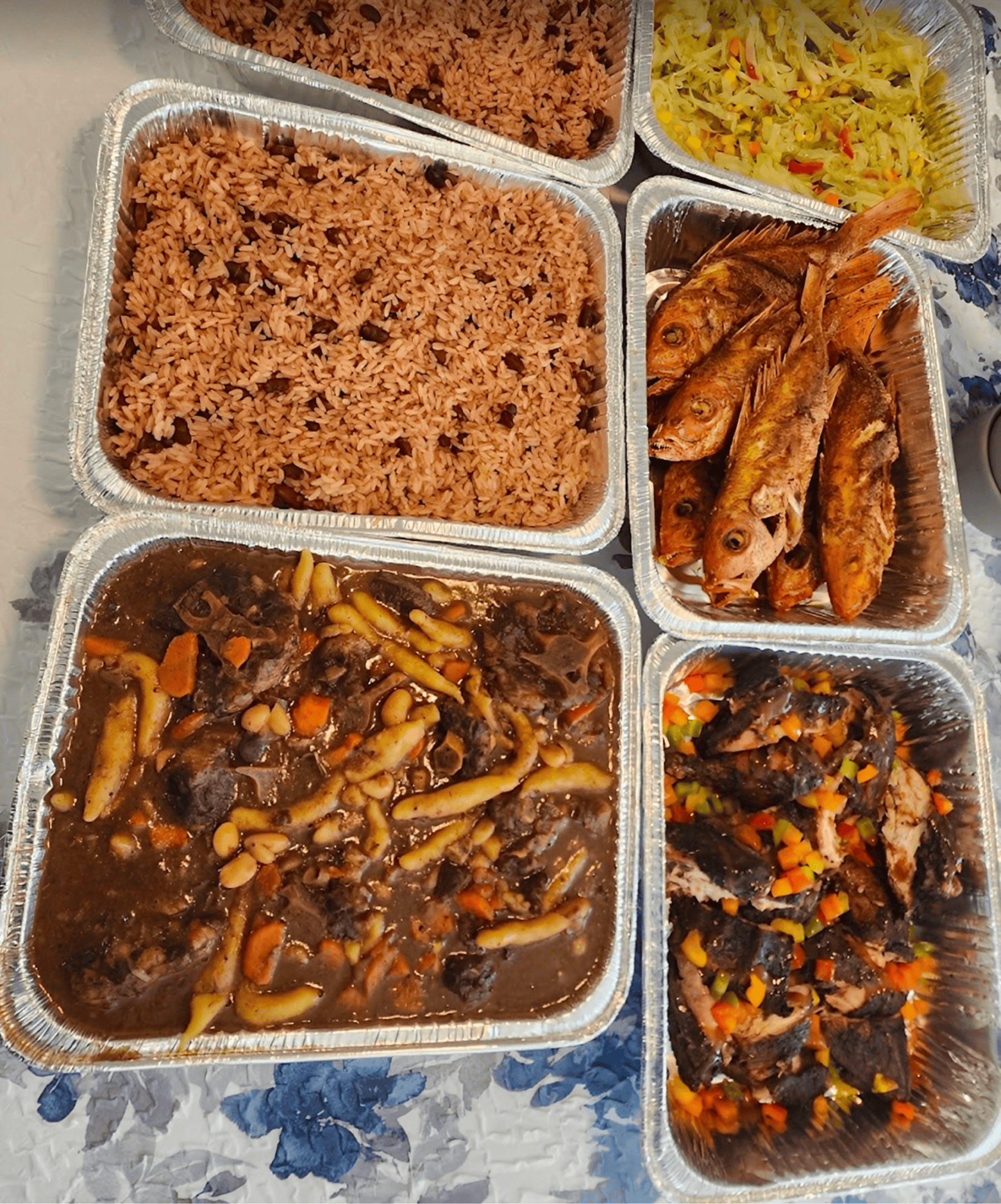 Foil trays with rice, fried fish, and stews