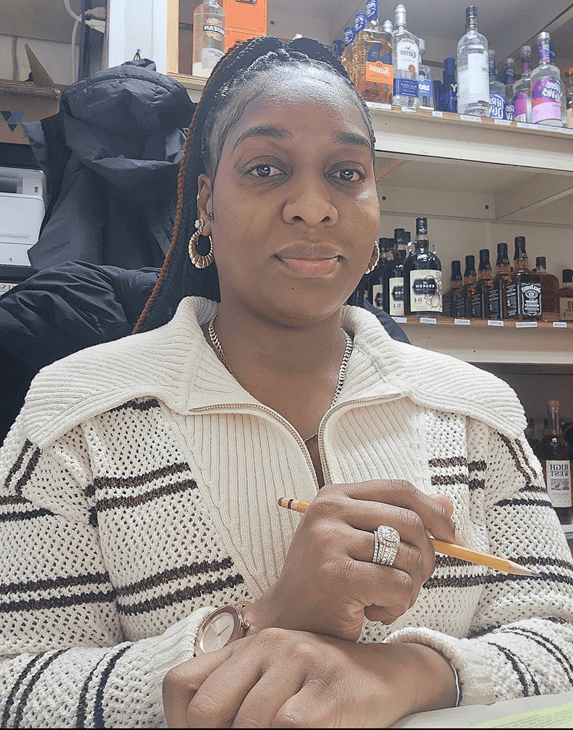 Woman at counter holding pencil, liquor bottles